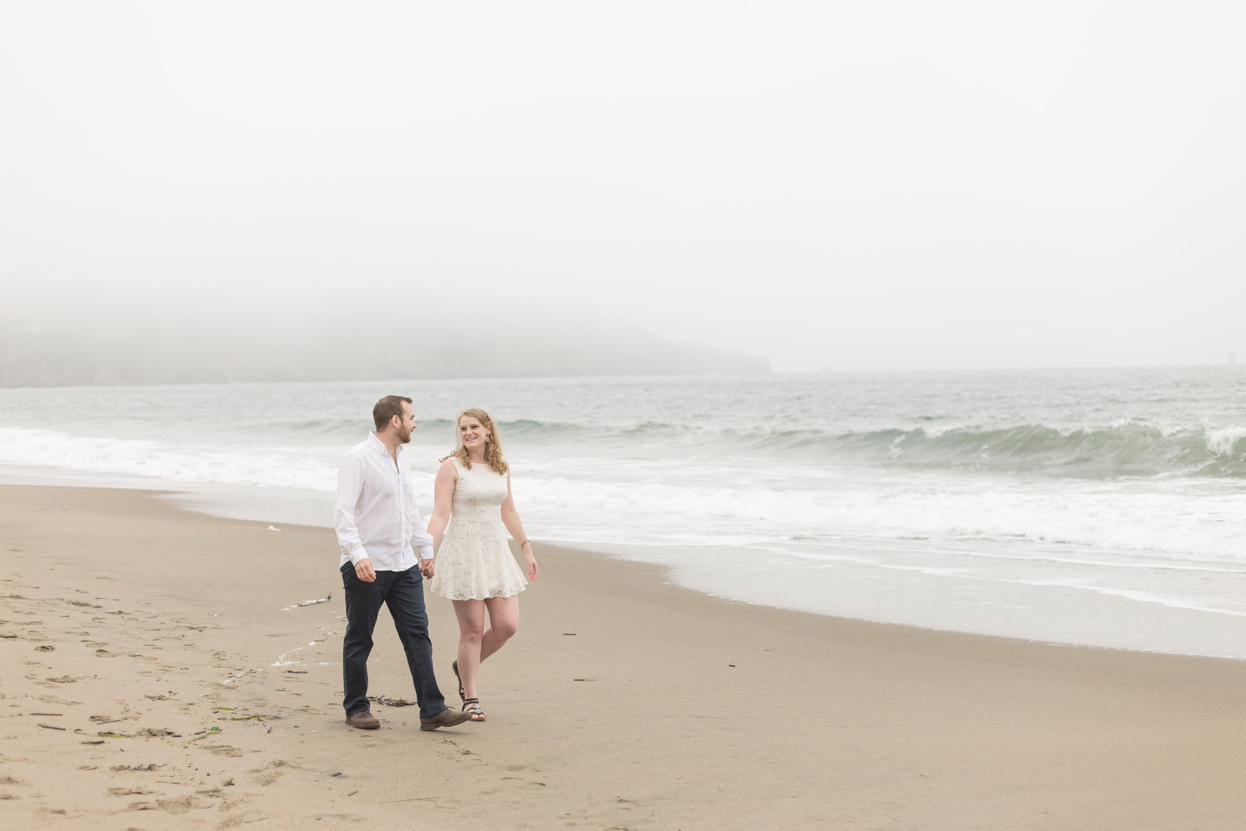 Husband and wife walking on the foggy beach in formal clothes