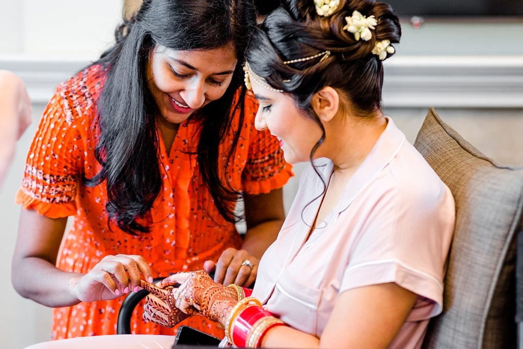 Bride and friend looking at henna designs on the morning of her wedding, shot by Amber Rivas Photography