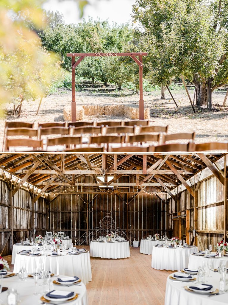 Wedding decorations setup at The Orchard in Watsonville, CA. The barn set up with white floor length tablecloths and rose centerpieces. Ceremony aisle leading to the arch with hay bales under it.