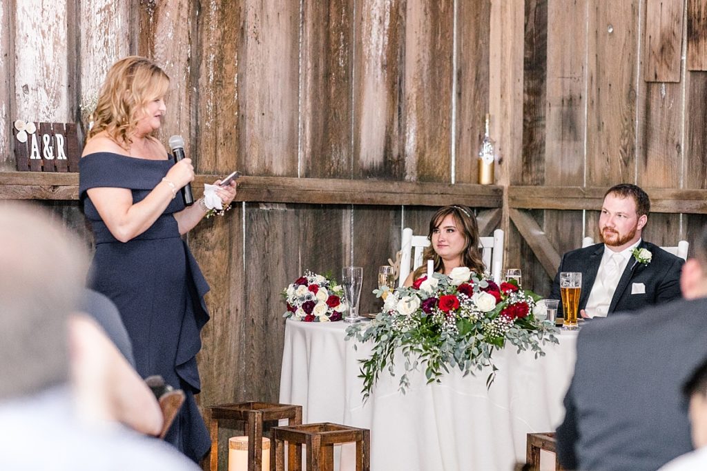 Bride's mother gives speech during wedding reception, bride cries as she listens.