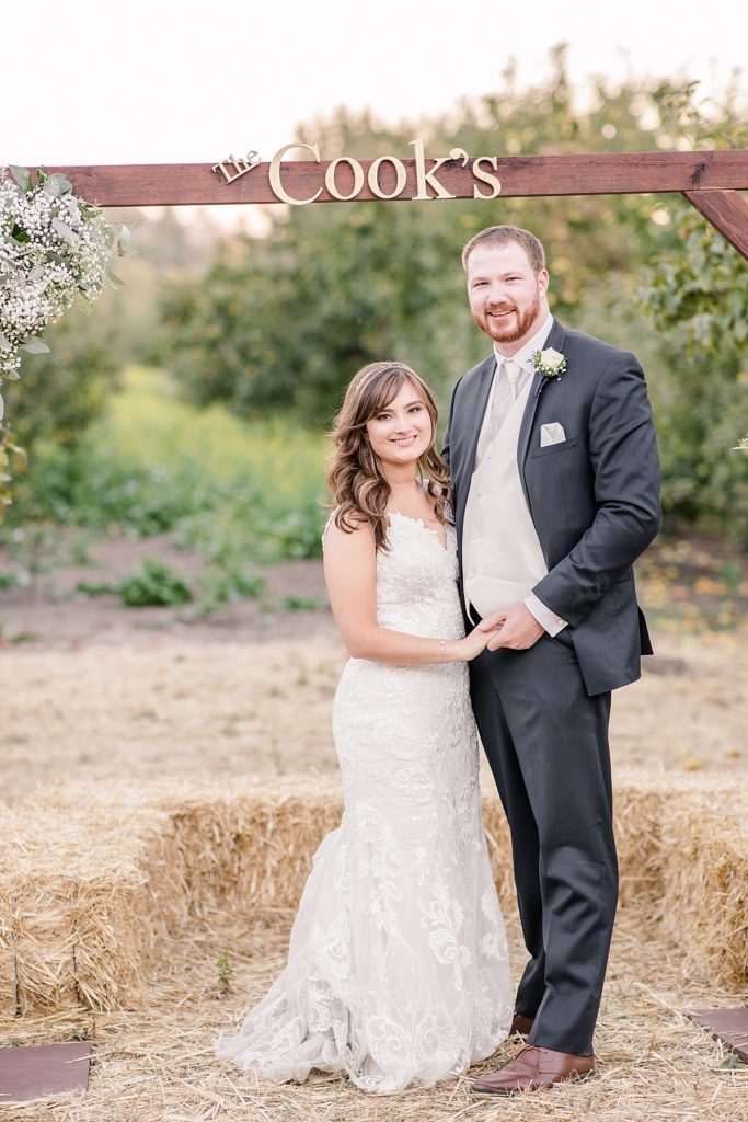 Bride and groom smile under their wedding arch in the apple orchard at The Orchard in Watsonville, CA.