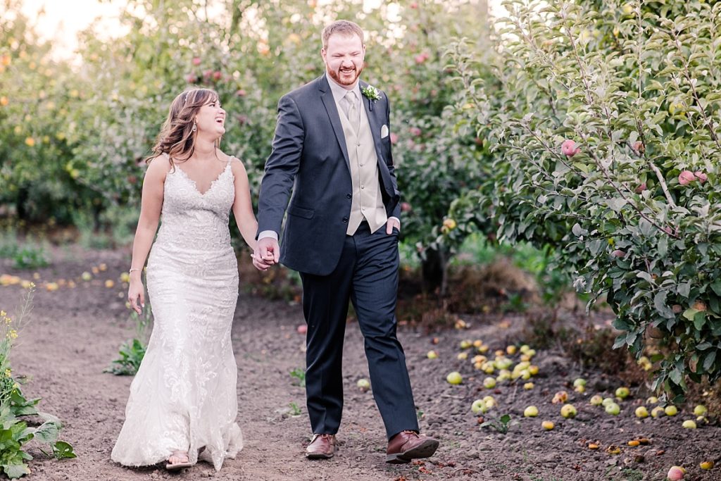 Bride and groom walking and laughing in the apple orchard at their fall wedding at The Orchard in Watsonville, CA. Shot by Amber Rivas Photography.