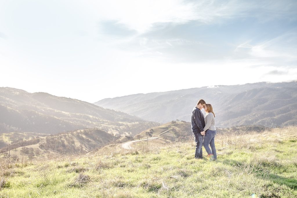 Del Valle engagement photos by Livermore photographer. Couple sunlit standing at Top of the Hill overlooking hills.