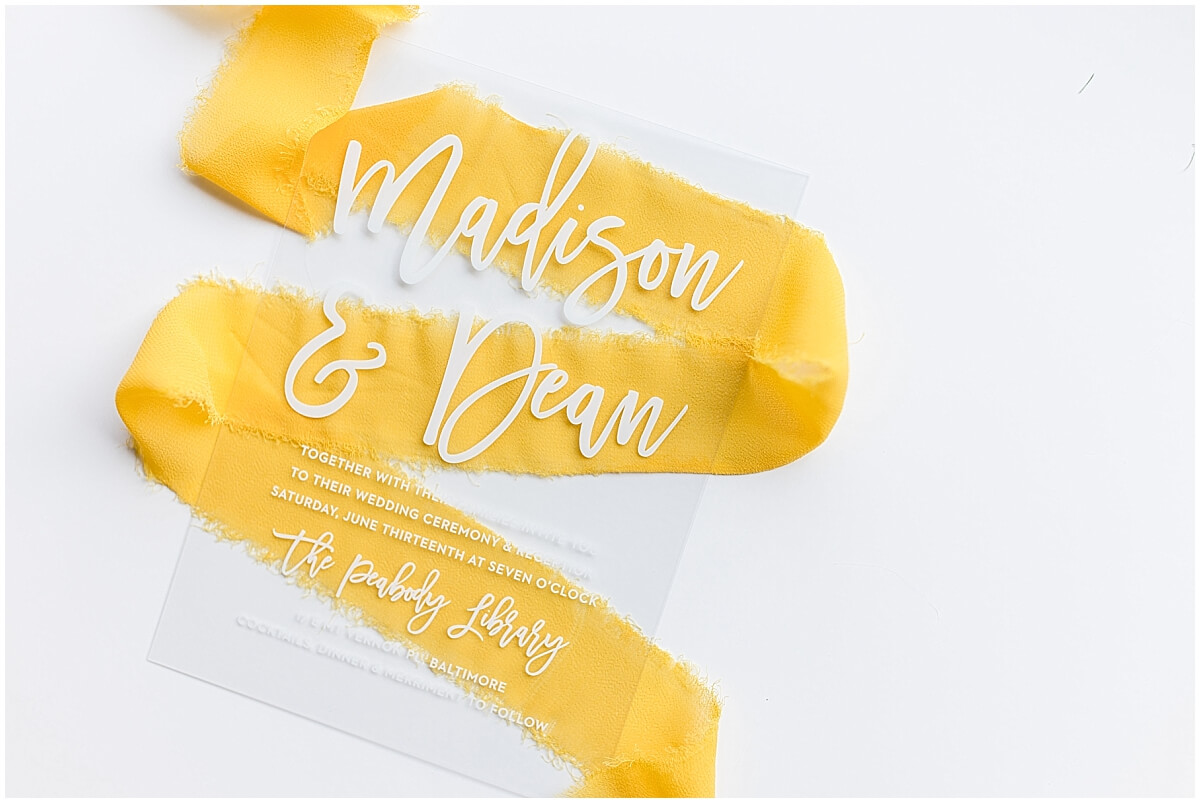 Clear wedding invitation with white script, styled with yellow ribbon