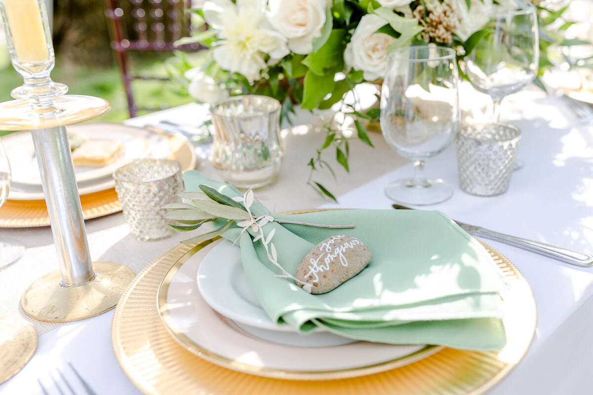 Elegant place setting with gold charger, white plates, pastel green cloth napkin, and scripted name setting on a rock