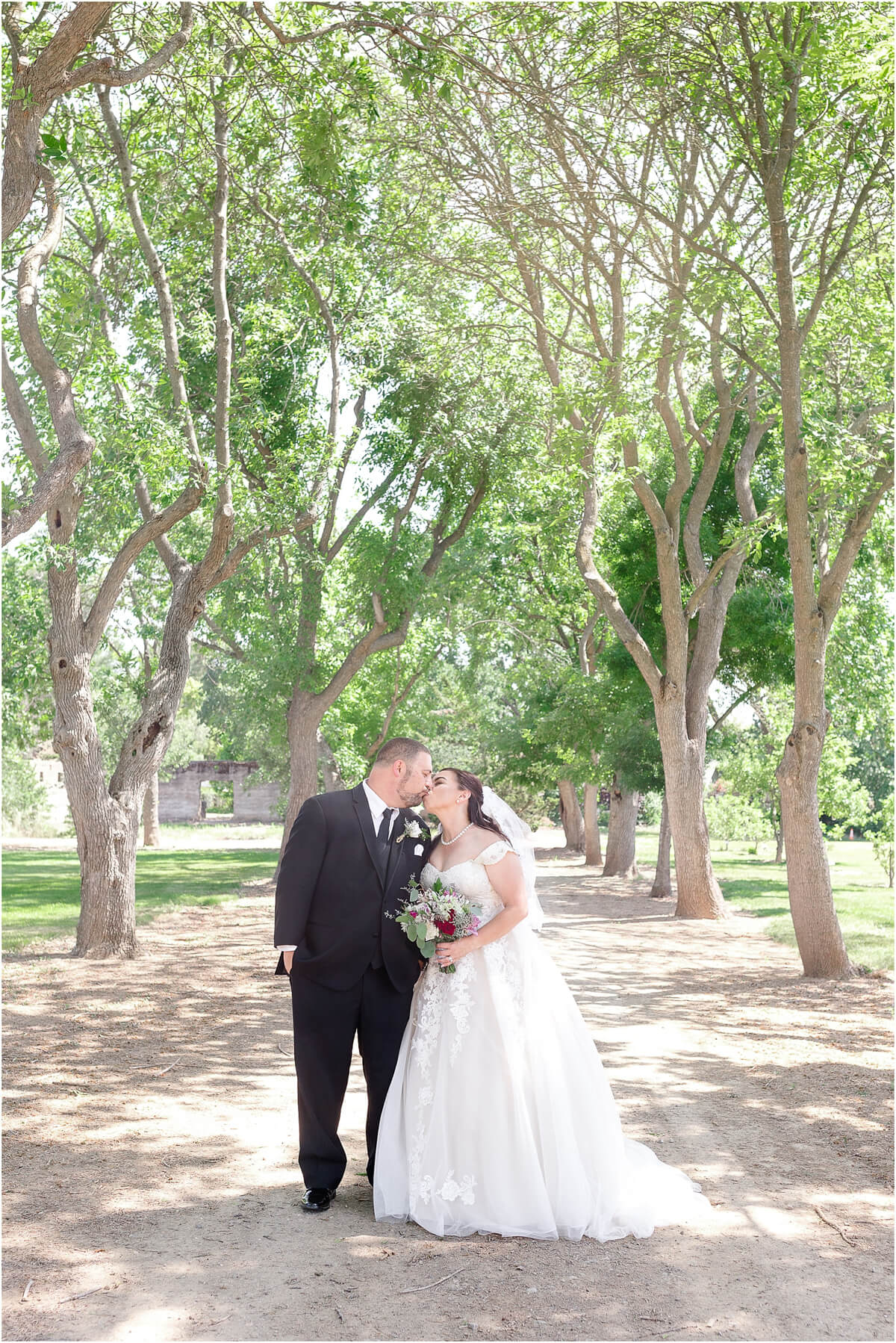 Bride and groom kiss under tree path at Ravenswood summer wedding